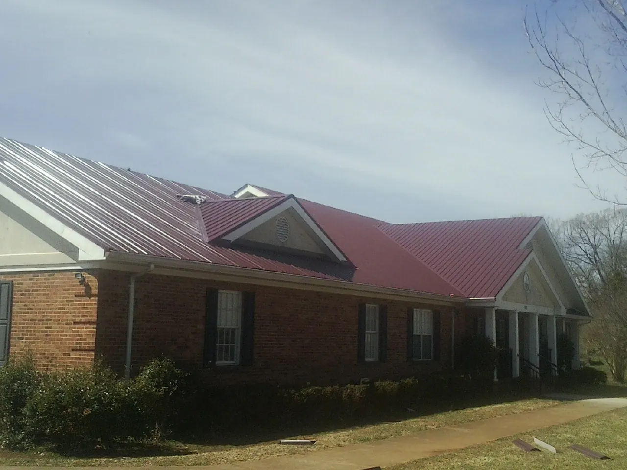 Red metal roof with gabled entries on a long brick building, from a Hail Damage Roof Repair job in Finleyville