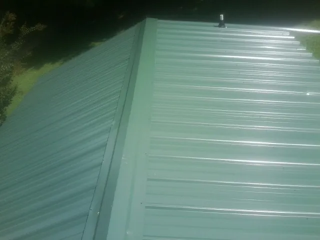 New green metal panels meeting at the ridge of a roof — Flat Roof Repair work by our crew in Finleyville