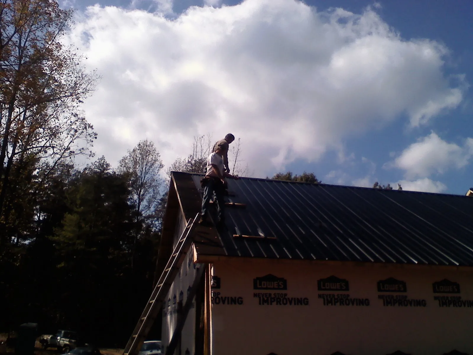 Roofer fastening dark metal panels high against a cloudy sky, from a Roof Inspection job in Finleyville