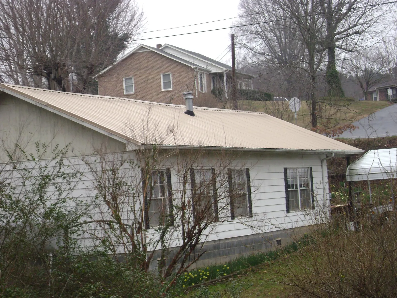 Tan metal roof on a white sided house set into a hillside — Commercial Roofing by Roofing Brothers in Finleyville
